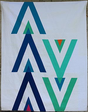 67 Degrees of Minimalism quilt front. Shades of blue and team triangle/arrow shapes on a white background with pops of pink and orange.