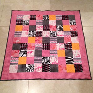 A pink and black patchwork baby quilt, with pops of orange.
