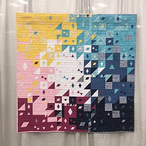 A colorful modern quilt with triangles and parallelograms hanging in a quilt show.