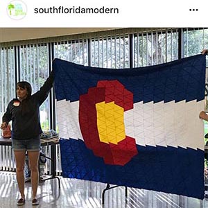 Sarah holding her finished Colorado flag quilt top at show and share with South Florida Modern Quilt Guild