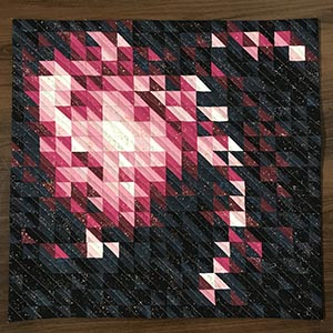 A mini quilt made of half square triangles that looks like a galaxy.