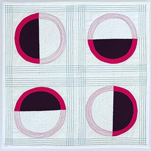 A modern mini quilt with four maroon and pink half circles on a white background.